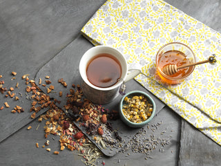 Slate with herbs and dried flowers, bowl of honey and a bowl of chamomile flowers, mug of herbal tea