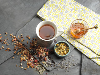 herbal cup of tea on a gray background with herbs and flower, yellow fabric and honey jar