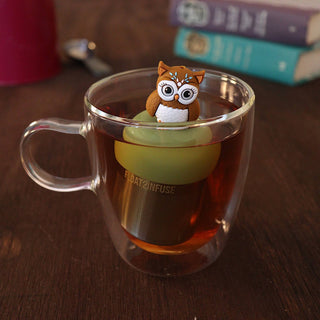 Clear glass mug with owl-shaped tea infuser on a wooden surface