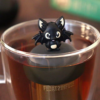 Black bat-shaped tea infuser in a glass mug with a blurred background