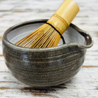 Ceramic matcha bowl with a bamboo whisk on a wooden surface