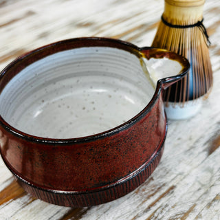 red matcha bowl with bamboo whisk on wooden table