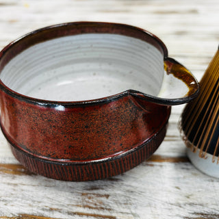 red matcha bowl with bamboo whisk on wooden table
