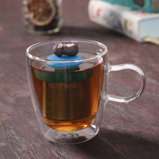 Clear glass mug with tea and a floating tea infuser on a wooden surface