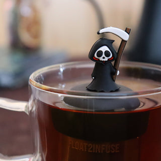 Grim Reaper-shaped tea infuser on a glass mug with a blurred background