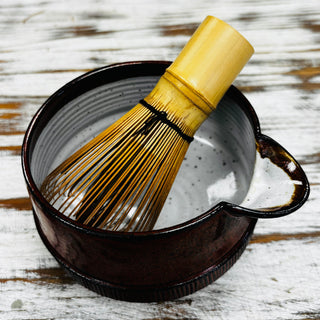 Bamboo whisk and matcha ceramic bowl on a wooden surface