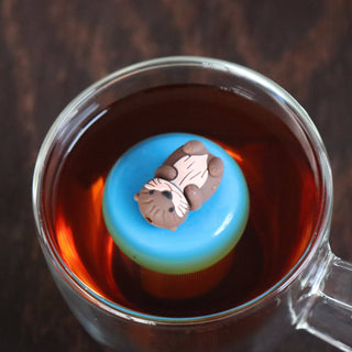 Tea bag with a blue label featuring an animal design in a glass of tea.