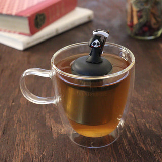 Clear mug with a tea infuser shaped like a skeleton on a wooden surface.