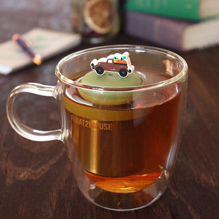 Clear glass mug with tea and a decorative tea infuser on a wooden surface.
