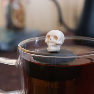 Skull-shaped tea infuser in a cup of tea with a blurred background
