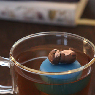Tea infuser shaped like an otter in a glass of tea on a wooden surface